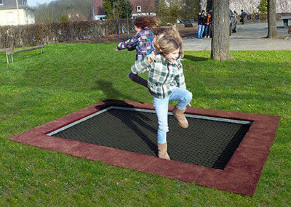 Zwei Kinder springen auf dem ebenerdig eingegrabenen Bodentrampolin von ATP Keiner